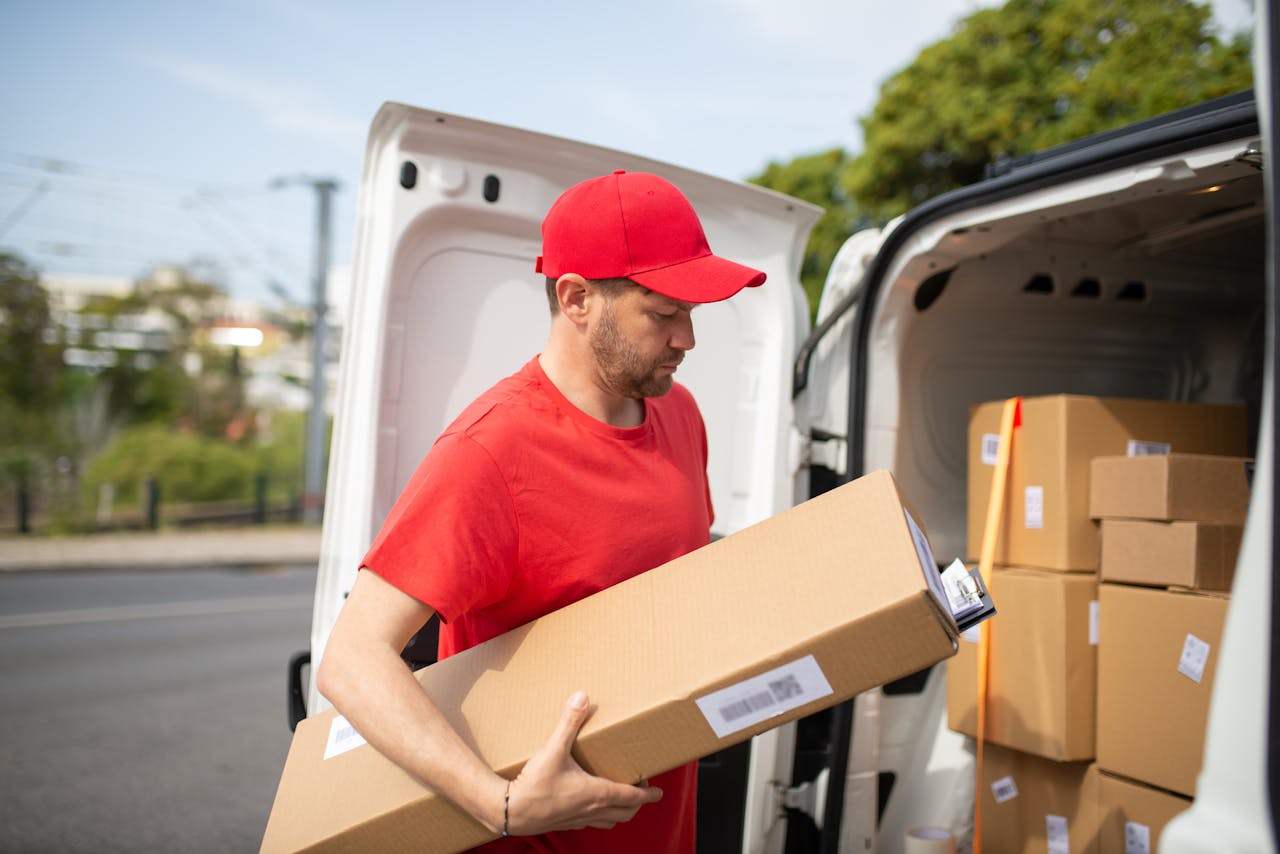 why-choose-us Courier in red uniform unloading packages from a delivery van on a sunny day.